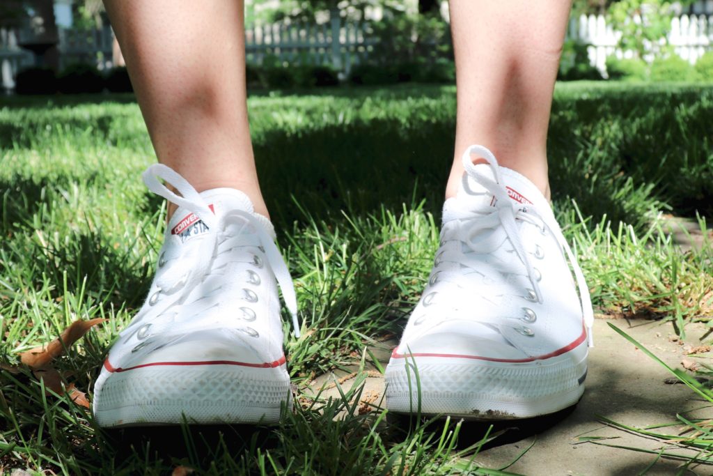 White quirky girl converse on young tan legs in a grass garden white picket fence fashion blog spring summer stone step